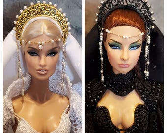May include: Two fashion dolls with elaborate headwear. One doll has a gold crown with pearl accents and a white veil. The other doll has a black crown with pearl accents and a black veil. Both dolls have dramatic eye makeup and long lashes.