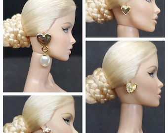 May include: A collection of images featuring a doll with blonde hair and different heart-shaped earrings. The earrings are gold-coloured and adorned with pearls and crystals. The doll has striking eye makeup and a side-swept updo hairstyle.
