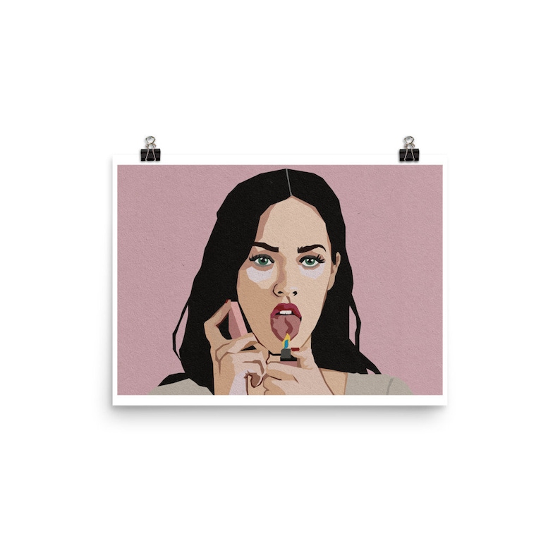 May include: Art print featuring a stylized illustration of a woman with black hair, green eyes, and a pink background. The woman is holding a lighter to her tongue. The print is secured with two black binder clips.