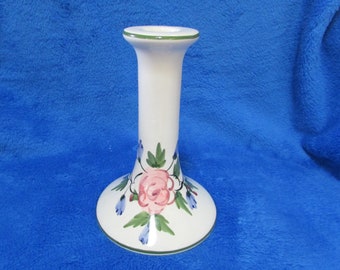 May include: White ceramic candle holder with a green rim and floral design. The design features a pink rose with green leaves and blue flowers.