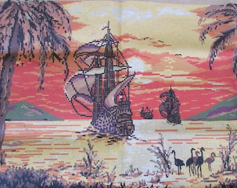 May include: A cross-stitch embroidery depicting a sunset scene with two ships sailing on the water. Palm trees are on either side of the scene, and there are birds flying in the sky. The sky is a vibrant orange and pink, and the water is a light blue.