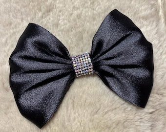 May include: A black satin bow with a clear rhinestone embellishment. The bow is perfect for adding a touch of elegance to any outfit.