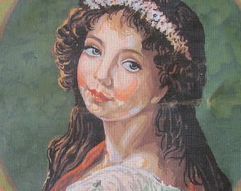 May include: A needlepoint portrait of a young woman with long brown hair wearing a white dress and a floral crown. The background is a green circle with a brown border.