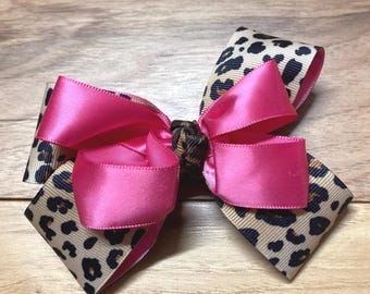 May include: A handmade hair bow featuring a combination of pink satin ribbon and leopard print ribbon. The bow is tied in a classic style, with the pink ribbon forming the center and loops, and the leopard print ribbon creating the base.