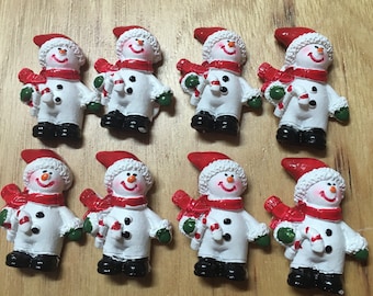 May include: Eight white snowman ornaments with red hats, white fur trim, and candy cane accents. The ornaments are decorated with black eyes, red cheeks, and black buttons.