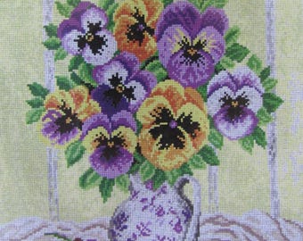 May include: A bouquet of purple, yellow, and white pansies in a white and purple patterned vase. The vase is sitting on a table with a white cloth.