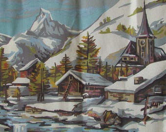 May include: A painting of a snowy mountain village with a church in the background. The church has a tall steeple and a pointed roof. There are several houses in the village, some with snow-covered roofs. The painting is done in a style reminiscent of a cross-stitch pattern.
