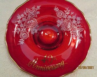 May include: A red glass plate with a gold rim and white floral design. The plate has a raised center and the words "40th Anniversary" written in gold script.