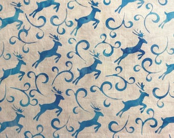 May include: A fabric with a repeating pattern of blue reindeer silhouettes and swirling decorative elements on a cream-colored background. The reindeer are depicted in a leaping pose.