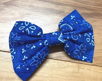May include: A blue bow tie with a paisley pattern. The bow tie is made of fabric and has a classic bow shape. The background is a wooden surface.