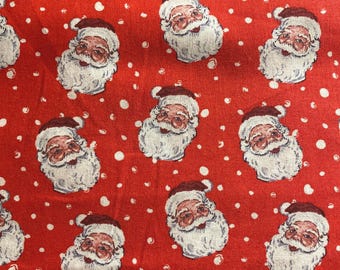 May include: Red fabric with a repeating pattern of Santa Claus faces and white polka dots. The Santa faces have white beards and red hats. This festive fabric is suitable for Christmas-themed crafts and projects.