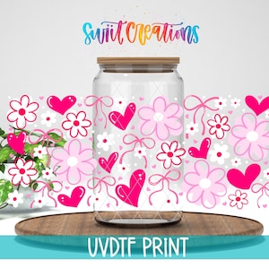 a glass jar with a lid, decorated with pink hearts, flowers, and bows, placed on a wooden surface.