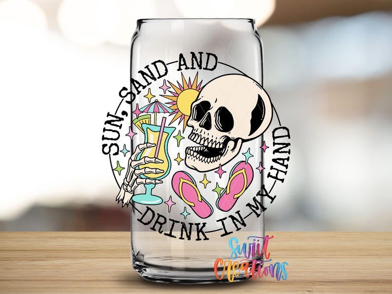 A glass with a colorful design featuring a skull, sunglasses, a beach umbrella, and a cocktail glass, along with the text "Sun, sand, and drink in my hand".