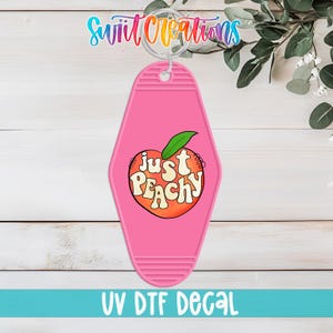Puede incluir: Llavero rosa estilo motel con diseño de melocotón y la frase "Just Peachy" en fuente retro. El llavero tiene un aro metálico y el texto "UV DTF DECAL" en la parte inferior.