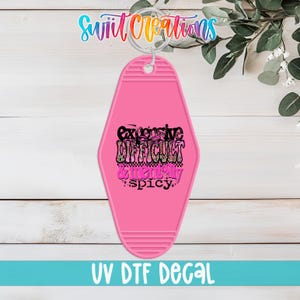 May include: A pink motel-style keychain with the words "Expensive, Difficult, & Mentally Spicy" in a retro font. The keychain has a silver ring and the text "UV DTF DECAL" at the bottom.