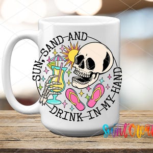 A white ceramic mug with a colorful design featuring a skull, sunglasses, and a beach scene, along with the text "Sun, sand, and drink in my hand".