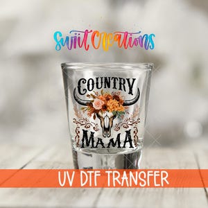 Puede incluir: Un vaso de chupito transparente con las palabras "COUNTRY MAMA" en escritura negra, con una calavera de toro con detalles florales. El vaso de chupito tiene el texto "UV DTF TRANSFER" en naranja. El logotipo "Sweet Creations" está en el fondo.