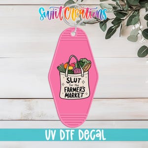 May include: A pink motel-style keychain with a white tote bag graphic filled with produce. The tote bag has the text "SLUT for the FARMER'S MARKET". The keychain also has the text "UV DTF DECAL".
