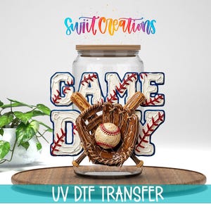 May include: A baseball-themed design featuring the words "GAME DAY" in a baseball stitch font, with a baseball, glove, and bats. The design is set against a clear jar with a wooden lid. The text "UV DTF TRANSFER" is at the bottom.