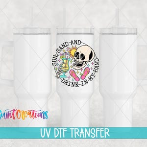 three white tumblers with a colorful design on the center, including a skull and a sun-like symbol. The text "Sun-Sand-And Drink-In My Hand" is displayed on the tumbler.