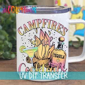 A white mug with a colorful design featuring a tequila bottle, cocktail glass, and campfire, along with the text "CAMPFIRE'S and Cocktails" and "UV DFT TRANSFER".