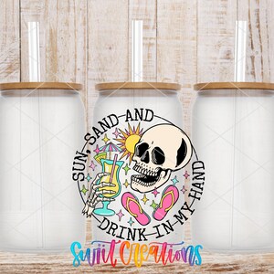 three clear glass jars with lids, each containing a straw. The jars are arranged in a row, and there is a colorful design on the front of one of them. The design includes a skull, a sun, and various other elements, creating a whimsical and playful appearance. The text "SUN, SAND, AND DRINK IN MY HAND" is prominently displayed on the front of the jar, suggesting a fun and lighthearted theme.