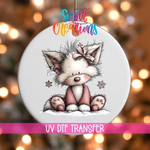 May include: A round white ceramic ornament featuring a cartoon illustration of a fluffy fox with a pink bow on its head, sitting in the snow with two snowflakes. The text "Swift Creations" appears at the top and "UV DTF TRANSFER" at the bottom.