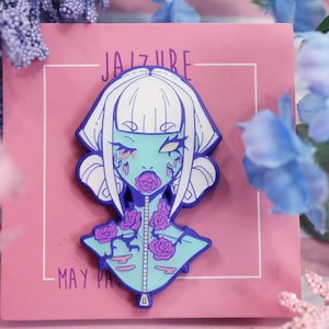 May include: A blue and white enamel pin featuring a cartoon character with white hair, blue skin, and a zipper down the front of their chest. The character has a rose in their mouth and roses are growing from their chest. The pin says "JAIZURE MAY PAY" at the bottom.