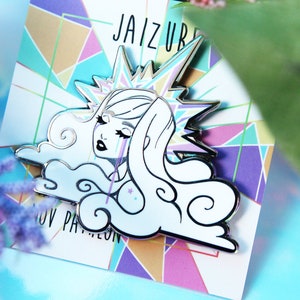 May include: A white and silver enamel pin featuring a stylized illustration of a woman with flowing hair, tears, and a starburst crown. The pin is set against a geometric background with the text "JAIZURI" and "NOV PANTHEON".