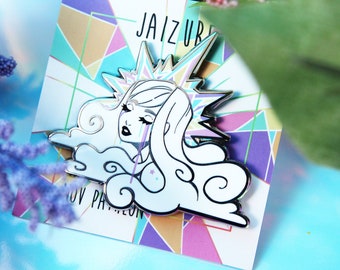 May include: A white and silver enamel pin featuring a stylized illustration of a woman with flowing hair, tears, and a starburst crown. The pin is set against a geometric background with the text "JAIZURI" and "NOV PANTHEON".