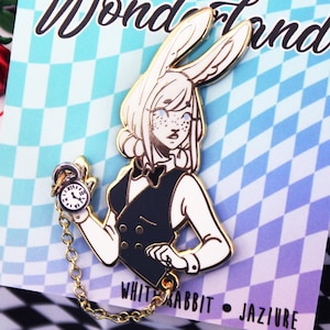 K&ouml;nnte beinhalten: Goldene Emaille-Anstecknadel mit einem wei&szlig;en Kaninchen, das einen Smoking tr&auml;gt und eine Taschenuhr mit Kette h&auml;lt. Das Kaninchen hat eine Fliege und einen wei&szlig;en, flauschigen Schwanz. Die Anstecknadel tr&auml;gt unten den Schriftzug "White Rabbit - Jazjure".