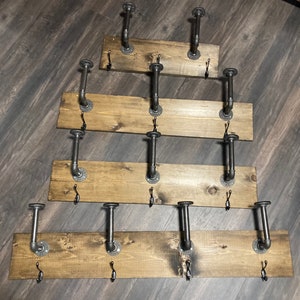 May include: Five wooden shelves with black metal pipe hooks. The shelves are stained a dark brown color and are arranged in a pyramid shape.