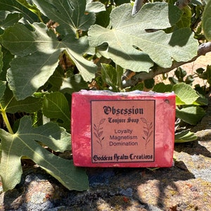 May include: A red bar of soap with the words "Obsession Conjure Soap" and "Loyalty Magnetism Domination Goddess Realm Creations" printed on the label.