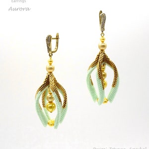 Könnte beinhalten: Goldene und hellgrüne Perlenohrringe mit einem hängenden Design. Die Ohrringe haben einen goldenen Hakenverschluss und sind mit kleinen goldenen Perlen verziert.