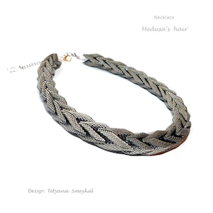 May include: A silver necklace with a braided design, called "Medusa's hair". The necklace is made of small, interconnected metal pieces that create a woven effect. The design is intricate and detailed, resembling a braid of hair. The necklace is a statement piece that would add a touch of elegance to any outfit.