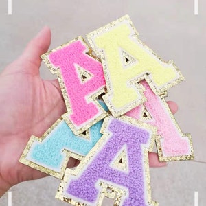 May include: A selection of colourful, fluffy letter "A" patches in pink, yellow, blue, purple, and light pink. Each letter has a gold glitter border. The image has the text "NICE DAY" and "80%" on the top.
