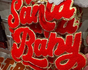 Peut inclure: Des patchs en feutre rouge avec des bordures dorées qui épellent "Santa Baby".