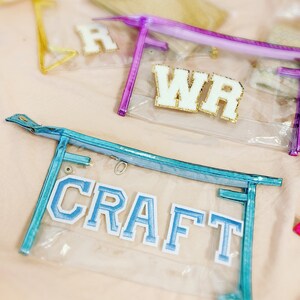 Puede incluir: Estuche de lápices de plástico transparente con una cremallera azul y un parche de fieltro azul que dice "CRAFT".