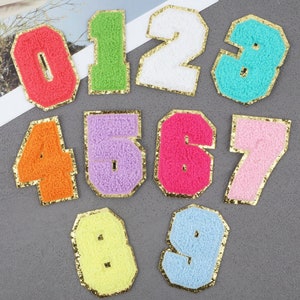 May include: Ten colorful felt patches shaped like numbers 0 through 9 with gold glitter trim. Each number is a different color.