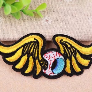 May include: Embroidered iron-on patch featuring a yellow and black winged eye with a red and blue iris.