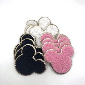 May include: A set of three felt Mickey Mouse head shapes with gold glitter trim. The shapes are black, pink, and white.