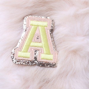 May include: A pink and green felt letter A with silver glitter. The letter is a patch or applique.
