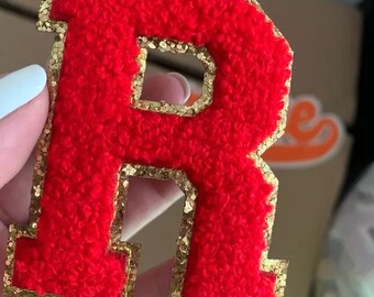 May include: Red felt letter R with a gold glitter outline. The letter is thick and fuzzy.
