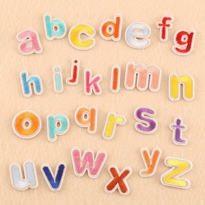 May include: A set of 26 colorful embroidered iron-on alphabet letters. Each letter is outlined in white and has a different color fill. The letters are arranged in alphabetical order.