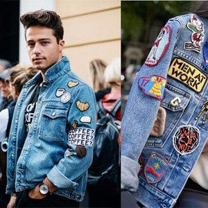 May include: Several light blue denim jackets are shown, each adorned with colorful patches. The patches feature various designs, including coffee cups, cartoon characters, and text like "MEN AT WORK" and "COOL". The jackets are styled in different ways, showcasing a trendy, personalized aesthetic.