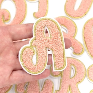 May include: A set of pink fuzzy letters with gold trim. The letters are in a cursive font and are perfect for adding a touch of whimsy to any project.