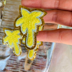 May include: A set of three yellow palm tree patches with a white outline and gold glitter trim. The patches are fuzzy and have a 3D effect.