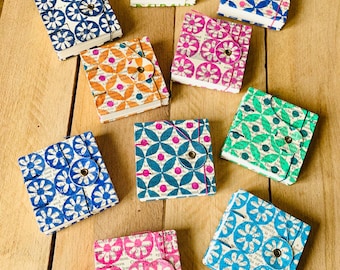 May include: A collection of nine square notebooks with covers made from printed book pages featuring various floral patterns in blue, green, pink, and orange. Each notebook is secured with a circular flap and a small metal fastener.