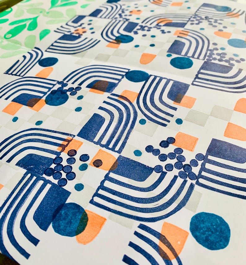 May include: A white paper sheet featuring a repeating pattern of dark blue arched lines, solid blue circles, clusters of small blue dots, and light orange semi-circles arranged in a grid-like layout with faint gray squares in the background.