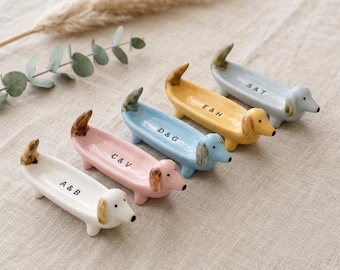 Può includere: Quattro poggia bacchette in ceramica a forma di bassotto nei colori bianco, rosa, blu e giallo. Ognuno presenta orecchie e coda marroni, con scritte nere: A & B, C & V, D & G, E & H e S & T su quello grigio. Hanno quattro piccole zampe.